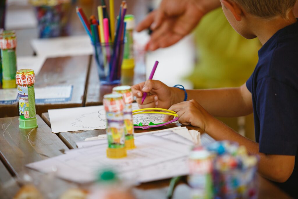 A young child focused on a drawing activity at a colorful art table indoors.