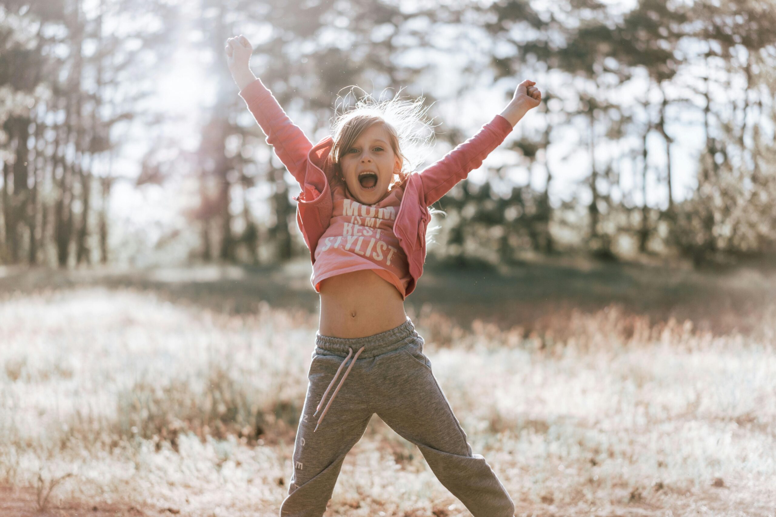A happy child in a red hoodie jumps with excitement in a sunlit field.